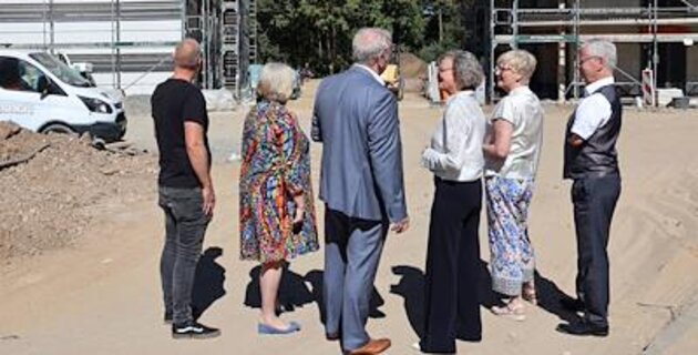 Besuchergruppe bei einem Baustellenrundgang zwischen zwei eingerüsteten Gebäuden eines Neubauprojekts