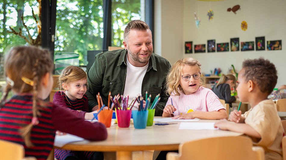Ein Mann sitzt zusammen mit mehreren Kindergartenkindern am Tisch