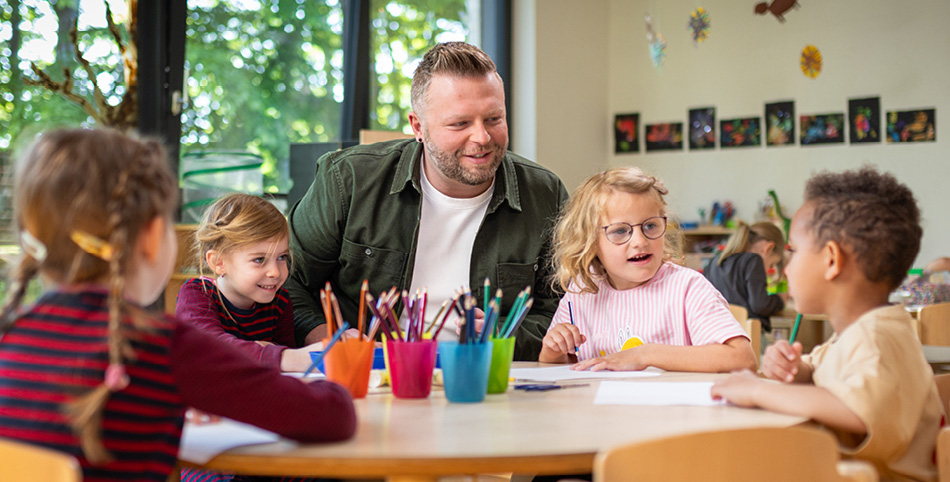 Ein Mann sitzt zusammen mit mehreren Kindergartenkindern am Tisch