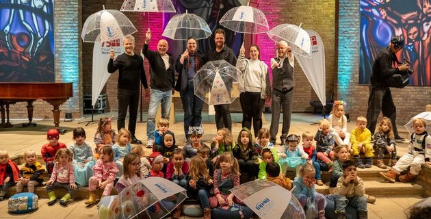 Kinder und Erwachsene stehen und sitzen in einer Kirche und haben einen Regenschirm in der Hand.