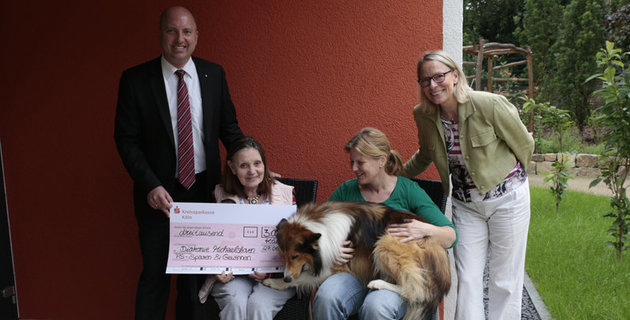 Mitarbeiter der Kreissparkasse Köln und der Diakonie Michaelshoven mit einem Therapiehund und einer Bewohnerin aus Michaelshoven.