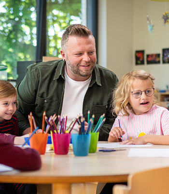 Ein Mann sitzt zusammen mit mehreren Kindergartenkindern am Tisch