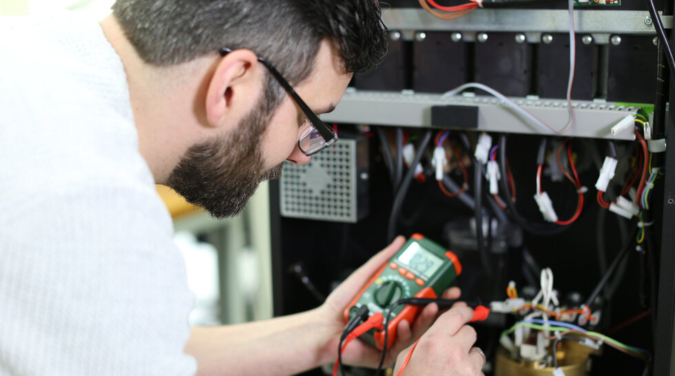Umschulung Elektroniker/-in Geräte Ein Mann prüft Kabel an einem Stromkasten