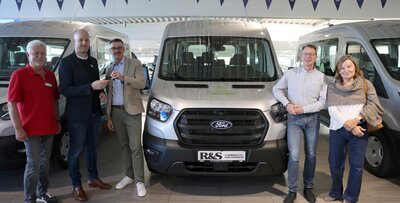 Ford Transit Vier Menschen vor einem großen Auto