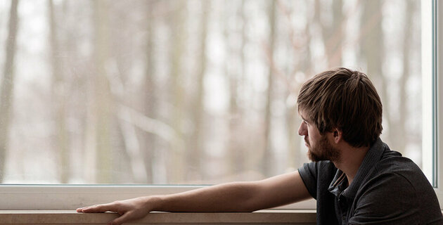 Ein junge Mann aus dem Autismus-Spektrum schaut aus dem Fenster.