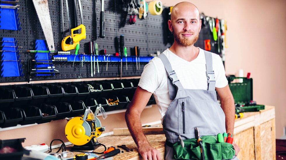 Ein Mann in Arbeitskleidung steht vor einer Werkbank mit Werkzeug