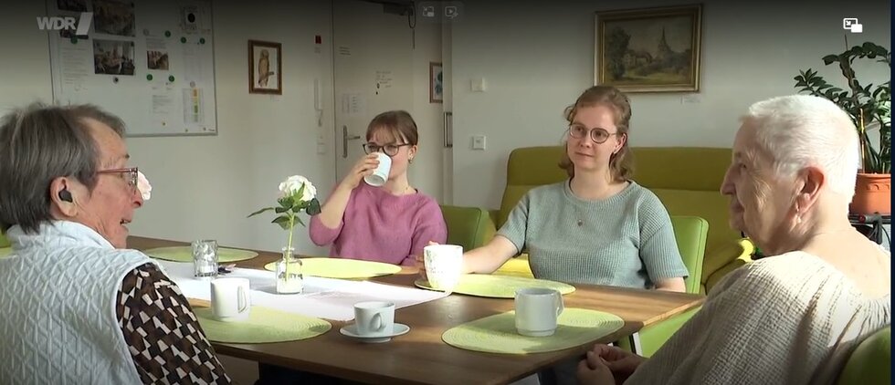 Zwei Senorinnen sitzen zusammen mit zwei Frauen am Tisch und trinken Kaffee