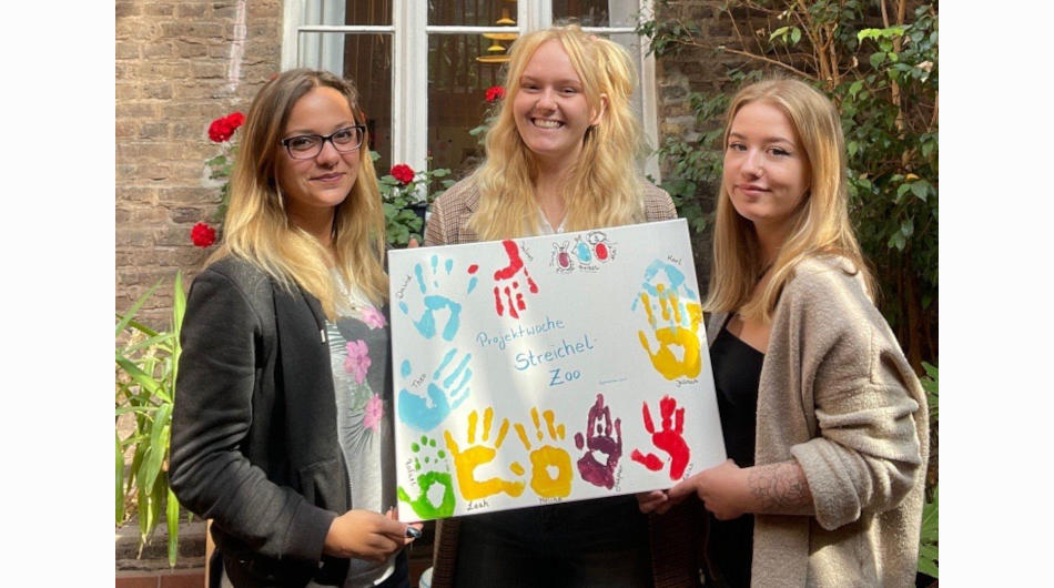 Projektarbeit in der FSH/O: Drei junge Frauen halten ein Bild mit bunten Handabdrücken.