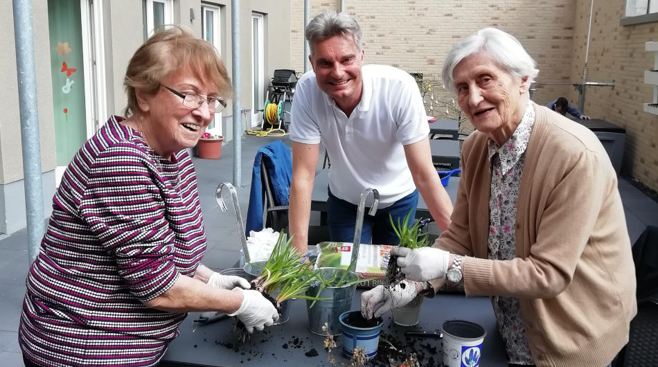 Tagespflege Sülz (Frühling) Zwei Kundinnen der Tagespflege Sülz und ein Mann pflanzen Blumen.