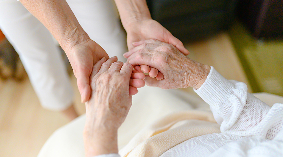 Eine Altenpflegerin hält die Hand einer älteren Bewohnerin