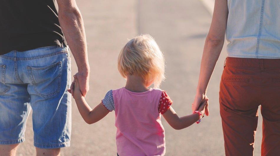 FamOus – Unterstützung für Familien in Oberberg: Eine Frau und ein Mann halten ein Mädchen an der Hand.