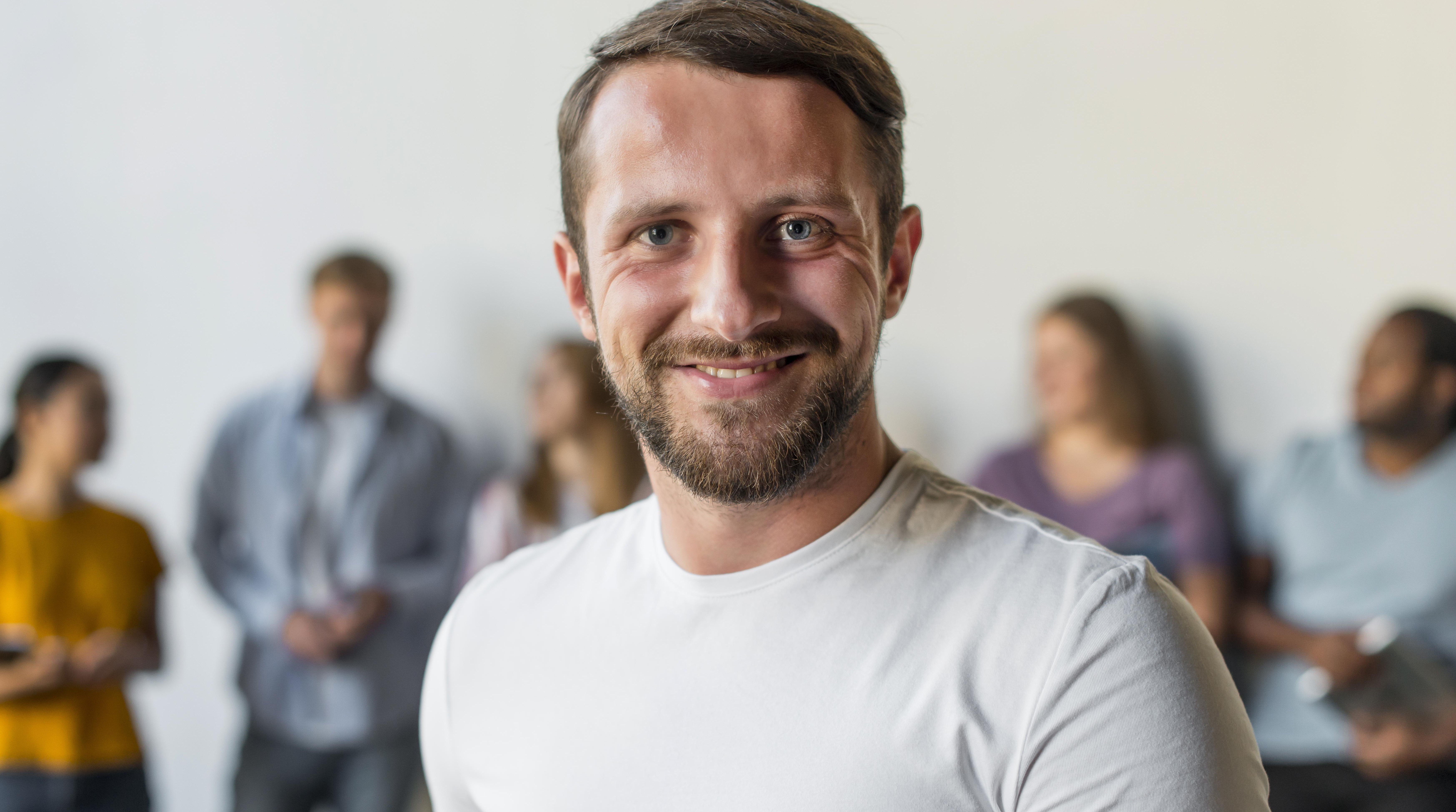 Ein Mann in weißem T-Shirt lacht in die Kamera