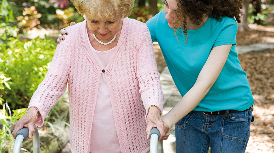 Sozialassistent/-in stützt eine Seniorin