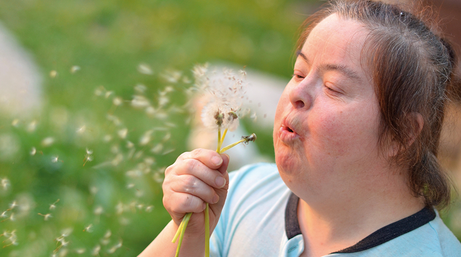 Hilfen für Erwachsene mit Behinderung Eine Frau mit Behinderung mit einer Pusteblume
