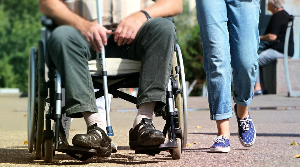 Case Management für migrierte Menschen mit Behinderung: Eine Person im Rollstuhl wird von einer gehenden Person begleitet.