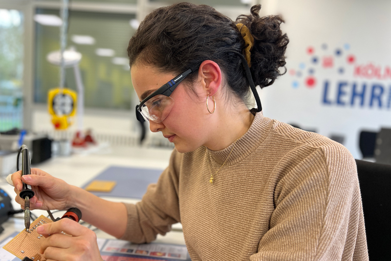 Nadja Graschi  Nadja Graschi sitzt am Tisch und lötet, sie hat eine Schutzbrille an.